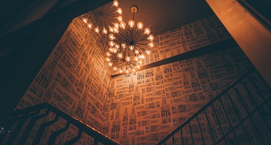 Stylish stairwell with chandelier and patterned wallpaper.